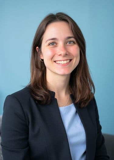 Example ERAS headshot — woman in navy blazer on pale-blue background, neutral lighting.